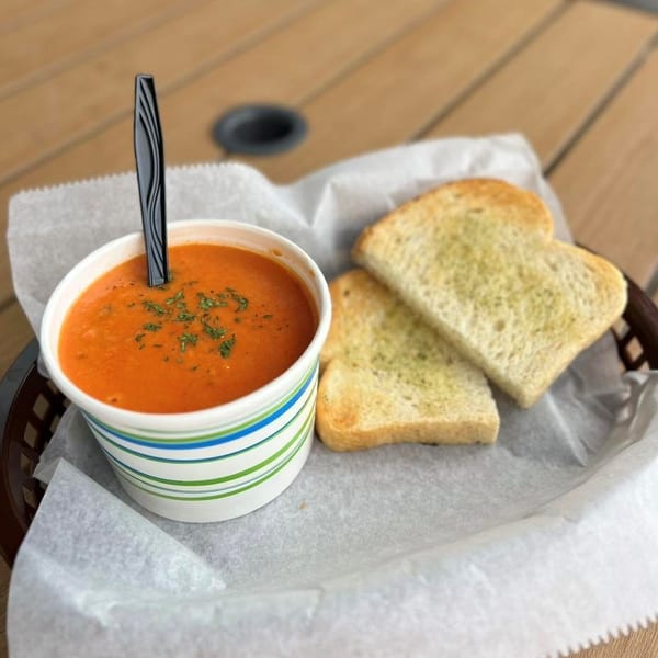 Tomato soup in a striped cup with a spoon and two slices of garlic toast in a basket.
