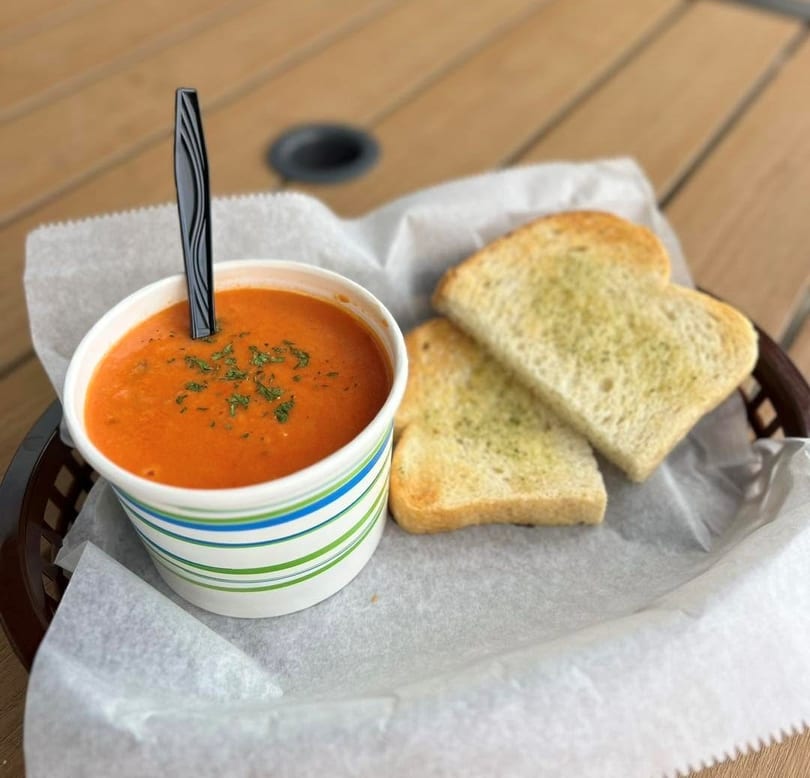 Tomato soup in a striped cup with a spoon and two slices of garlic toast in a basket.