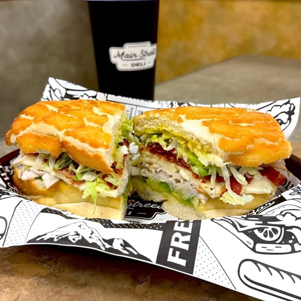 A Main Street Deli sandwich, cut in half, revealing turkey, bacon, avocado, lettuce, and cheese.